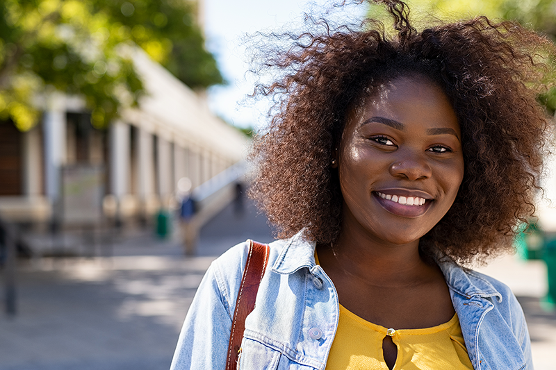 Portrait of young african american woman with curly hair smiling and looking at camera. College student on campus.