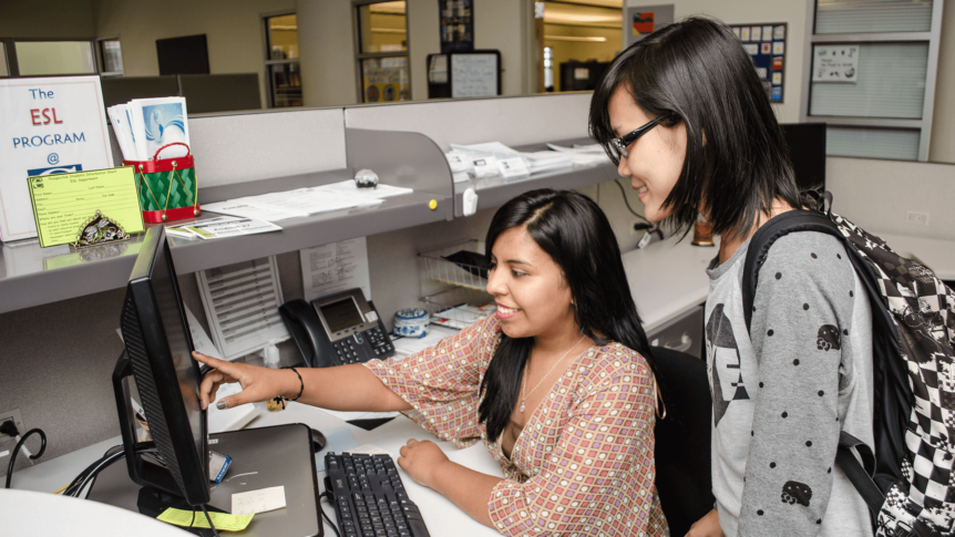 Smiling ESL Student Worker Points to Computer Desktop Screen